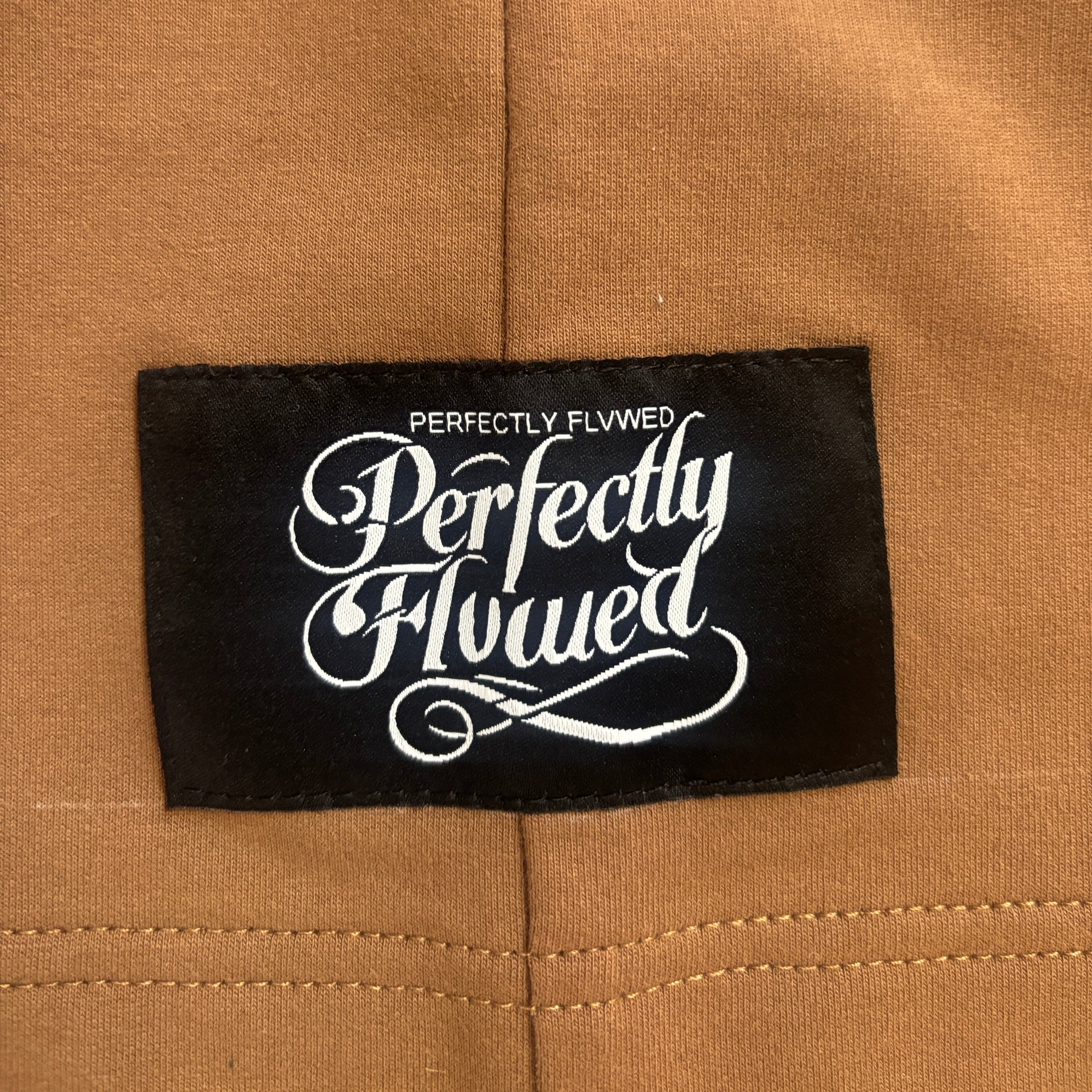 Label with 'Perfectly Flwwed' text on a brown fabric background